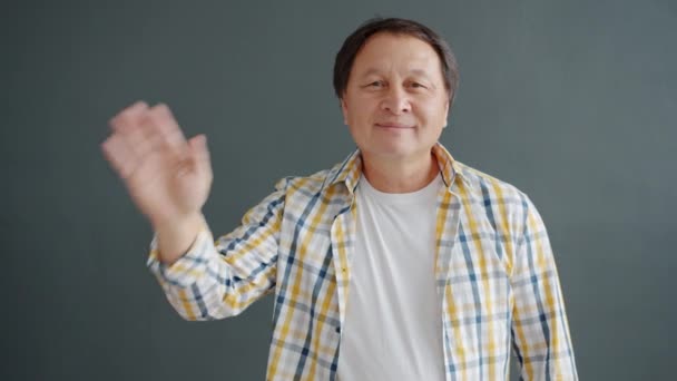 Cheerful mature Asian man waving hand smiling greeting people looking at camera — 비디오