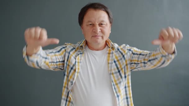 Lento movimento de homem asiático decepcionado mostrando polegares para baixo gesto de mão em estúdio — Vídeo de Stock