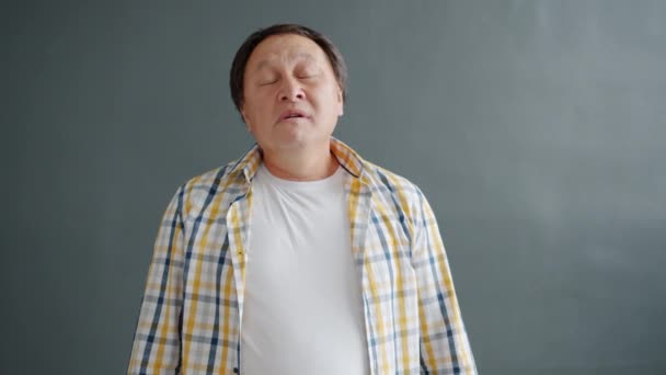 眠いアジア人男性yawning感じ疲れているか退屈立ち上の灰色の背景 — ストック動画