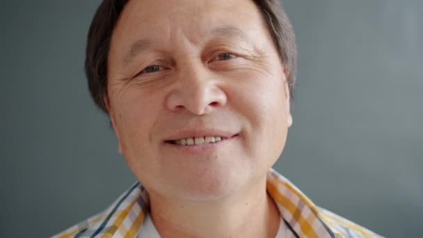 Збільшений повільний портрет веселої азійської людини, що посміхається на чорному фоні — стокове відео