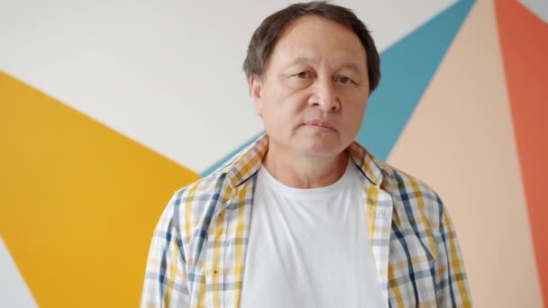 Portrait of Asian adult standing alone on colorful background looking at camera — Stock Video