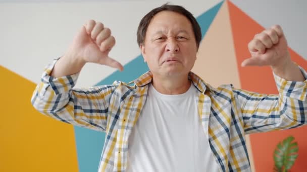 Divertido asiático chico mostrando los pulgares hacia abajo gesto de la mano sobre fondo colorido — Vídeos de Stock