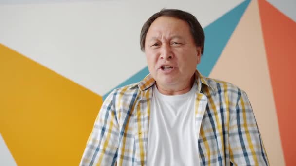 Dühös ázsiai srác kiabál gesztikulálva nézi a kamerát otthon állni — Stock videók