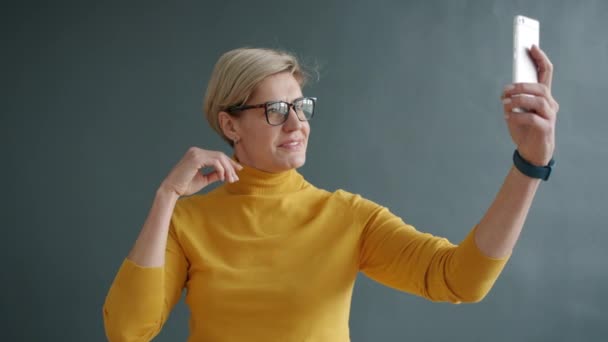 Portré vonzó felnőtt hölgy csinál szelfi okostelefon kamera a stúdióban — Stock videók