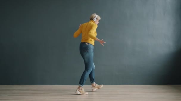Взрослая женщина в модной одежде танцует в студии в наушниках — стоковое видео