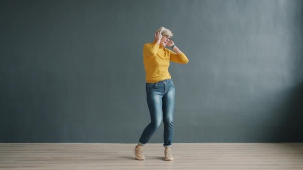 Señora despreocupada con auriculares bailando en el estudio disfrutando de la canción divirtiéndose sola — Vídeos de Stock