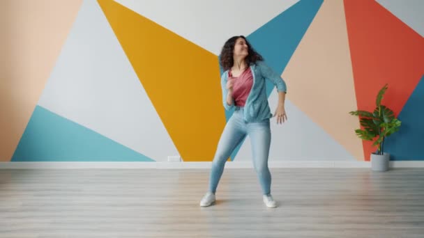 Chica alegre estudiante bailando en el interior del estudio disfrutando de la libertad y la música sonriendo — Vídeos de Stock