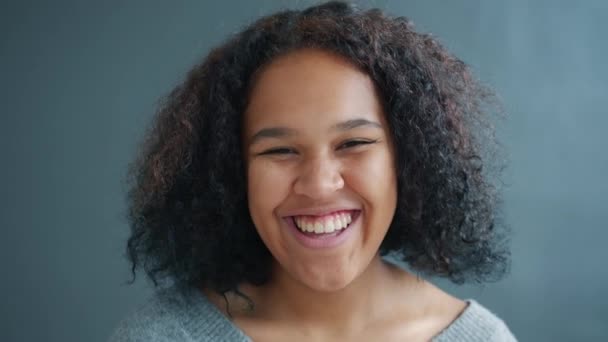 Close-up of cute Afro-American lady laughing standing on gray background — Stock Video