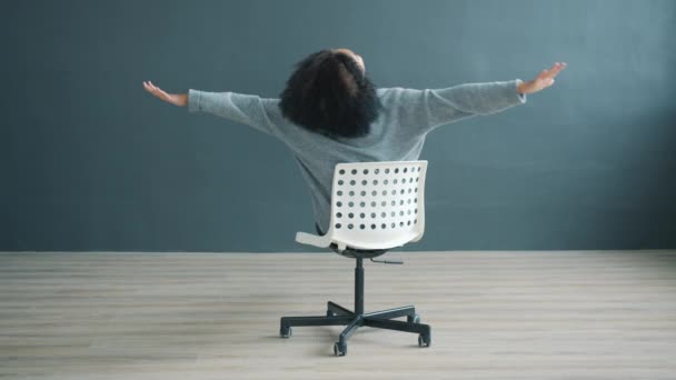 Portrait de fille afro-américaine ludique filant sur chaise de bureau sur fond gris — Video