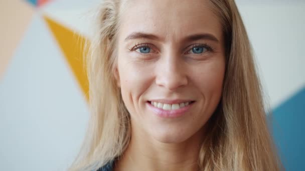 Gros plan portrait d'une fille unique aux yeux bleus et aux cheveux blonds souriants à l'intérieur — Video