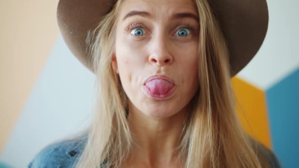 Porträtt av söt blond gör roliga ansikten bär hatt ha kul inomhus ensam — Stockvideo