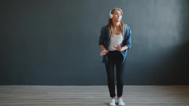 Mouvement lent de jolie jeune femme dansant portant des écouteurs sur fond sombre — Video