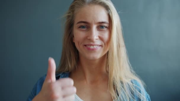 Joyeux jeune femme souriant montrant pouce vers le haut geste de la main sur fond gris — Video