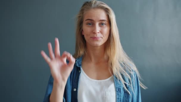 Retrato de una mujer guapa mostrando un signo de aprobación sobre un fondo gris sonriendo — Vídeo de stock