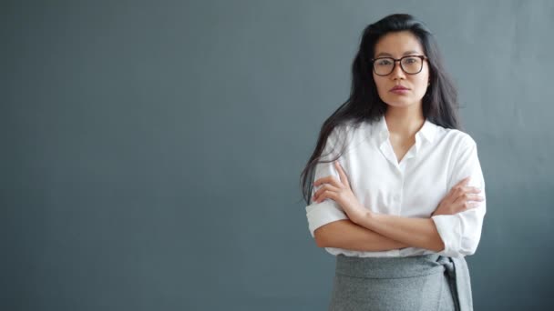 Retrato en cámara lenta de una mujer de negocios asiática seria de pie sobre fondo gris — Vídeos de Stock
