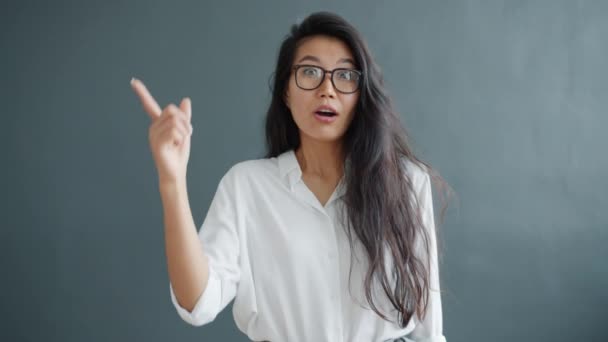 Cámara lenta de inteligente asiático chica levantando dedo teniendo buena idea en gris fondo — Vídeos de Stock