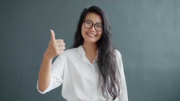 Feliz señora asiática mostrando el gesto de la mano pulgar hacia arriba sobre fondo gris oscuro — Vídeos de Stock