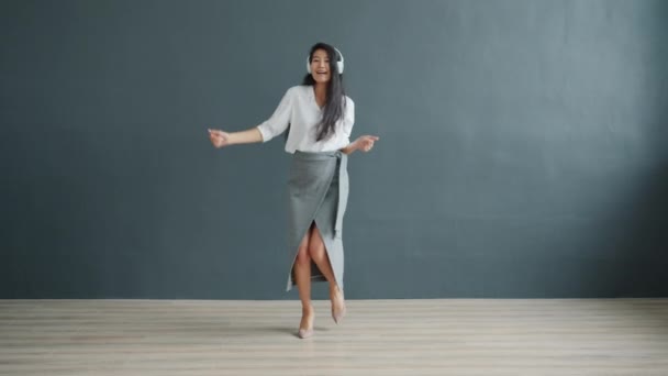 Uzun siyah saçlı neşeli Asyalı kadın kulaklık takarak dans ediyor. — Stok video