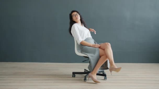 Pěkný asijské businesswoman spinning na židle indoors na tmavý šedý pozadí — Stock video