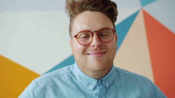 Porträtt av glad kille i trendiga glasögon ler på färgglada bakgrund — Stockvideo