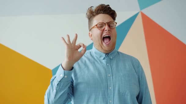 Fröhlicher Mann mit Brille zeigt Ok-Geste und zwinkert auf buntem Hintergrund — Stockvideo