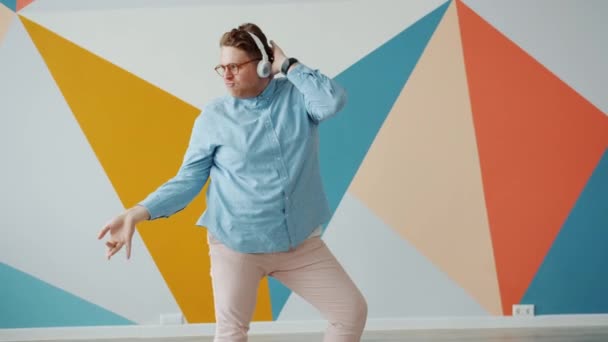 Playful young man dancing on colorful background wearing headphones enjoying music — 비디오