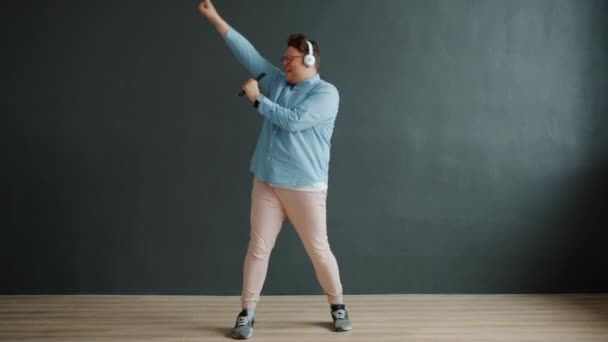 Vicces srác énekel táncol hallgat zenét keresztül fejhallgató sötét háttér — Stock videók