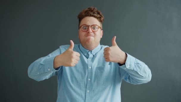 Pleased young man showing thumbs-up gesture with both arms on dark gray background — 비디오