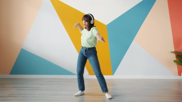 Мила молода жінка танцює в приміщенні на барвистому фоні в навушниках — стокове відео