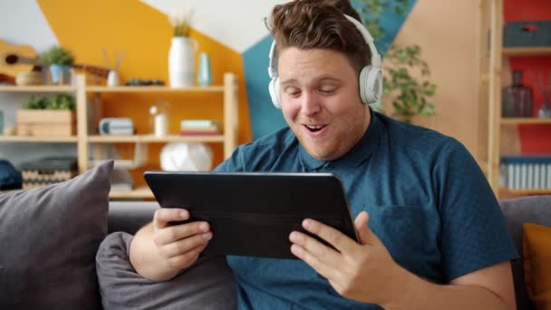 Przystojny facet cieszący się wideo na ekranie tabletu w słuchawkach w domu — Wideo stockowe