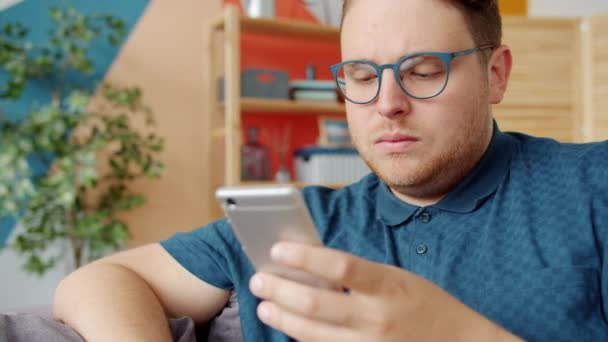 Fiatal férfi használ okostelefon komoly arc, majd mosolyog és nevet otthon — Stock videók