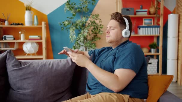 Sensible hombre moviendo brazos bailando escuchando música en auriculares usando smartphone — Vídeos de Stock