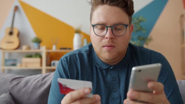 Jeune homme effectuant un paiement en ligne avec une carte de crédit touchant l'écran du smartphone — Video