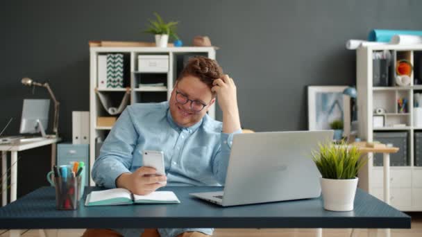 Felice ragazzo sms utilizzando smartphone sorridente lavorare da solo alla scrivania in ufficio — Video Stock