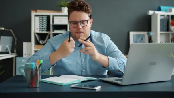 Langzame beweging van gekke jongeman kantoormedewerker die plezier heeft met pennen op het werk — Stockvideo