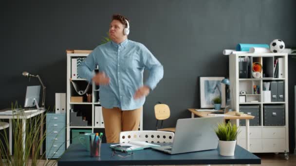Cámara lenta del trabajador de oficina feliz bailando escuchando música a través de auriculares — Vídeos de Stock