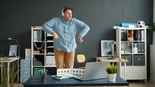 Медленное движение смешного сотрудника, танцующего в офисной комнате в наушниках — стоковое видео