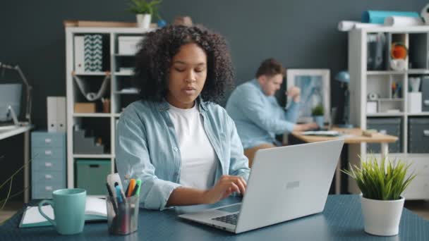 Afro-Amerikaanse kantoormedewerker met behulp van moderne laptop notities maken op het werk — Stockvideo