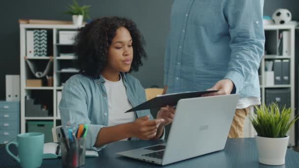 Senhora afro-americana atraente que toma documentos de colega masculino, em seguida, usando laptop — Vídeo de Stock