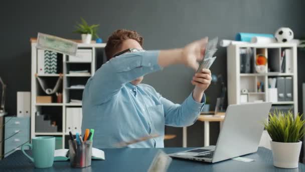 Успешный бизнесмен бросает деньги, веселясь за столом в офисе в одиночку — стоковое видео