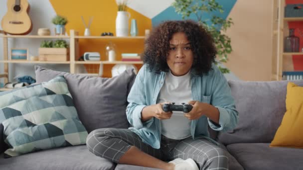 Portré fiatal afro-amerikai lány élvezi videojáték otthon ül a kanapén — Stock videók