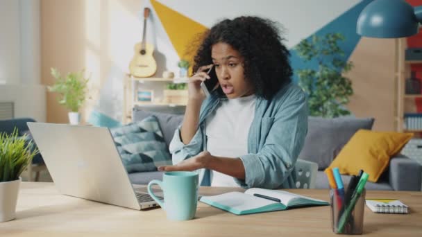 Çılgın Afro-Amerikalı kadın cep telefonuyla bağırıyor. Evde bilgisayarla çalışıyor. — Stok video