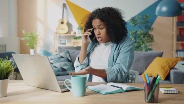 Őrült afro-amerikai nő kiabál mobilon, laptoppal otthon dolgozik. — Stock videók