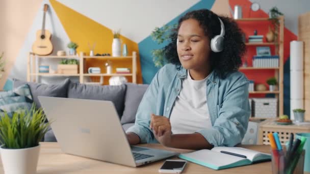 Linda senhora em fones de ouvido ouvindo música no apartamento apreciando a música digitando no laptop — Vídeo de Stock