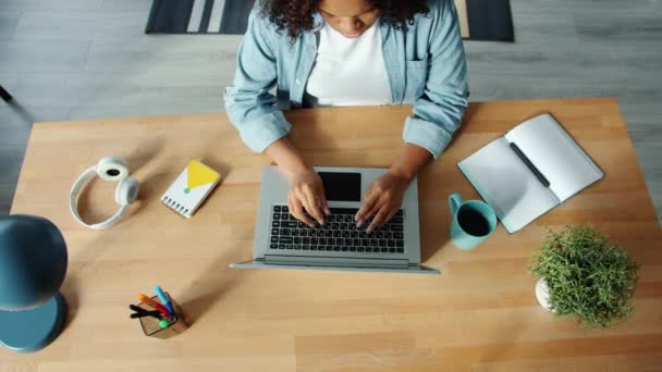 Vista superior de la mujer afroamericana que trabaja con el ordenador portátil en casa escribiendo — Vídeos de Stock