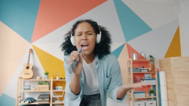 Portrait de fille attrayante dans les écouteurs chantant dans la danse à télécommande à la maison — Video