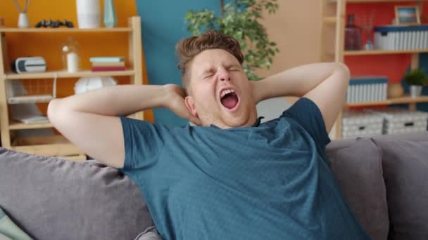 Sleepy student yawning stretching arms waking up after nap on sofa at home — Stock Video