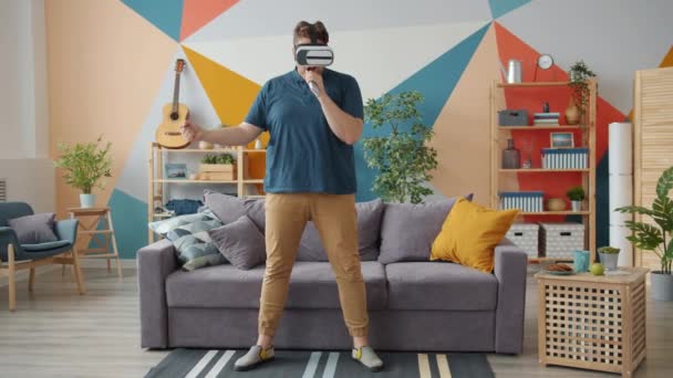 Creative man singing in remote control wearing virtual reality glasses at home — 비디오