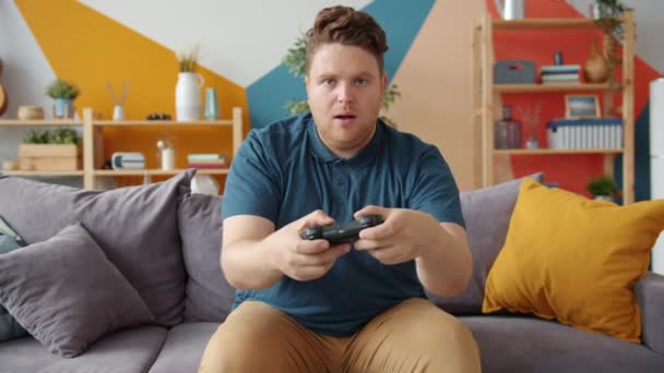 Emocional hombre disfrutando de videojuegos en casa sentado en el sofá en casa en el apartamento — Vídeos de Stock