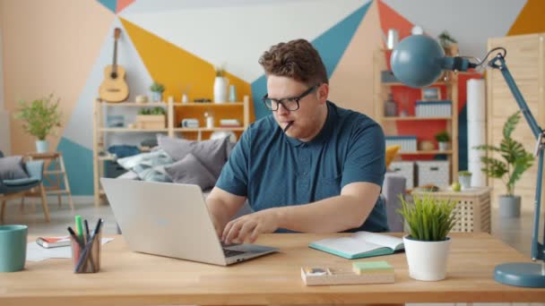 Retrato de un joven hombre de negocios que trabaja desde casa en línea utilizando el ordenador portátil tomando notas — Vídeo de stock
